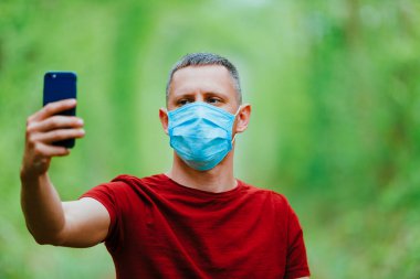 Bir adam ormanın arka planında maske takıp selfie çekiyor.