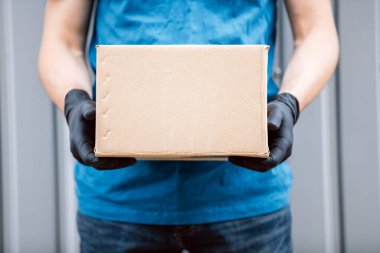 Eldiven takan ve koruyucu maske takan teslimatçı adam eve paket getiriyor..