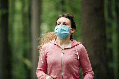 Tıbbi maskeli bir kadın ormanda koşuyor. Karantina sırasında formda kalın. Coronavirus salgını Covid-19