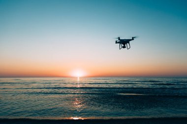 Deniz günbatımının arka planında uçan dron