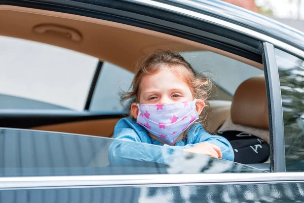 little girl in a medical mask from a car window. Hygiene mask protection coronavirus or covid-19