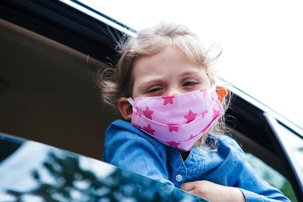little girl in a medical mask from a car window. Hygiene mask protection coronavirus or covid-19