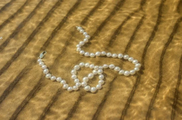 Pearl beads on the sea sand — Stock Photo, Image