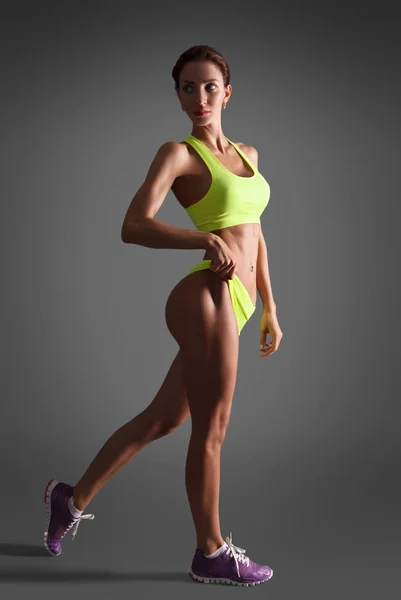 Мускулистая молодая спортсменка, оглядывающаяся назад на сером фоне — стоковое фото