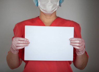 Kadın doktor eldiven ve koruyucu maske takıyor, elinde boş kağıt tutuyor..