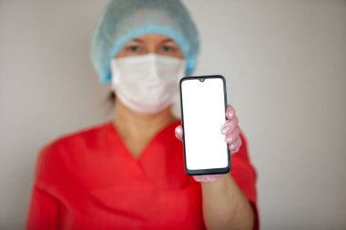 Kadın doktor eldiven ve maske takıyor, akıllı telefon tutuyor..