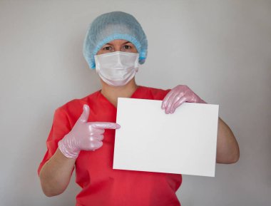 Kadın doktor eldiven ve koruyucu maske takıyor, elinde boş kağıt tutuyor..