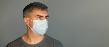 Koruyucu maskeli ve gri tişörtlü bir adam..