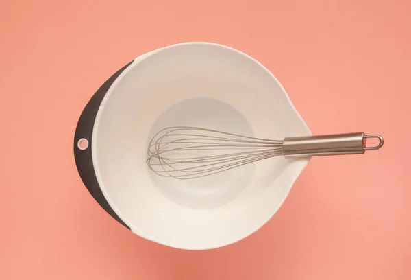 Whisk e uma xícara de plástico para chicotear em um fundo rosa . — Fotografia de Stock