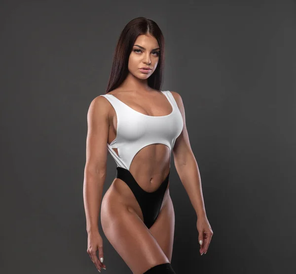 Mooie sexy brunette in een sport bikini op een grijze achtergrond. — Stockfoto