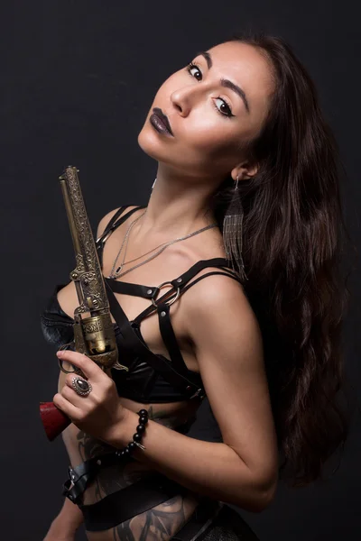 Sexy dziewczyna w czarnym bielizna i miecz pasa na szarym tle. W ręku trzyma vintage rewolwer — Zdjęcie stockowe