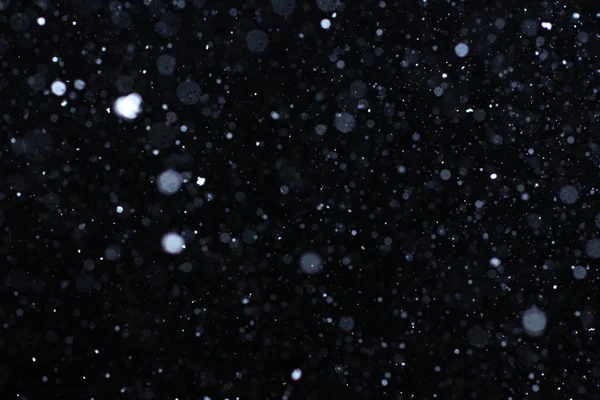 Snowstorm texture. Bokeh lights on black background, shot of flying snowflakes in the air — Stock Photo, Image