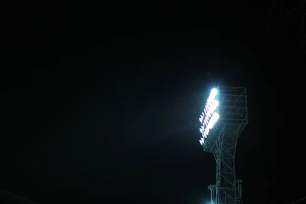 Bodové světlo věž stadionu během sněžení proti temné noční obloze na pozadí — Stock fotografie