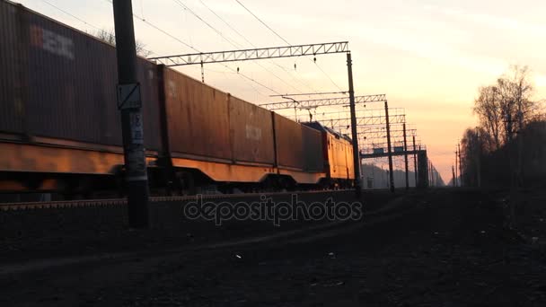 Um trem de carga está passando por uma estação rural sob a luz do pôr do sol . — Vídeo de Stock