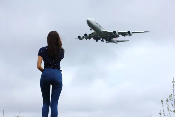 NOVOSIBIRSK - MAY 13: Woman spotter watching airplane outdoors in a summer field. Boeing 747 Cargolux landing at cloudy sky Novosibirsk Tolmachevo Airport. May 13, 2017 in Novosibirsk Russia — Stock Photo, Image