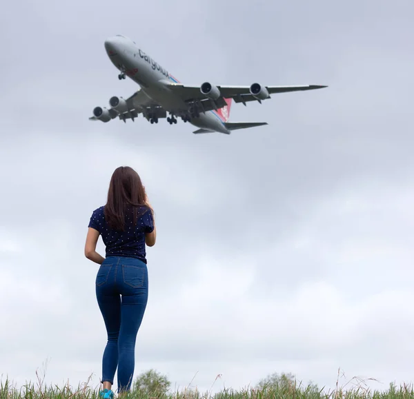 NOVOSIBIRSK - MAY 13: Woman spotter watching airplane outdoors in a summer field. Boeing 747 Cargolux landing at cloudy sky Novosibirsk Tolmachevo Airport. May 13, 2017 in Novosibirsk Russia — Stock Photo, Image