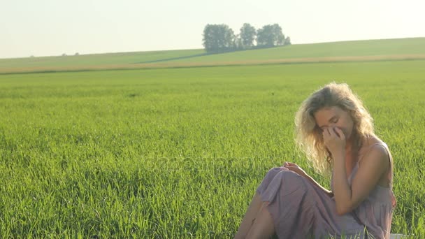 Chica en ropa de estilo boho relajarse tranquilamente mientras se sienta en un campo de hierba verde en una tarde de verano soleado — Vídeo de stock