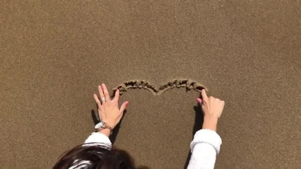 Main de femme dessinant le cœur sur le sable. vague de mer efface le dessin . — Video