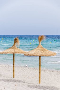 Kum plaj ve berrak gökyüzü hasır şemsiyeler.
