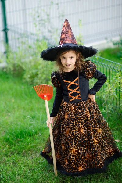 Vorbereitung auf Halloween. das Mädchen im Anzug der bösen Hexe reinigt eine Rasenharke — Stockfoto