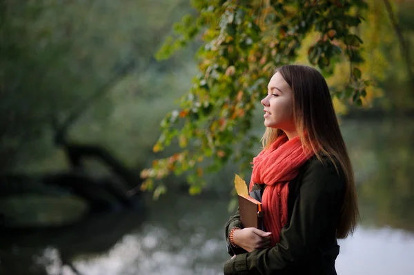 Mooi meisje met een heldere rode sjaal wandelingen in herfst park. — Stockfoto