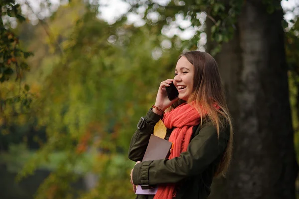 Lovely girl in bright red scarf is leaning against the trunk of a large tree. — Stock Photo, Image