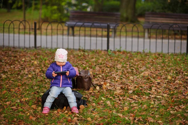 La niña se sienta en un césped en el parque de otoño . — Foto de Stock