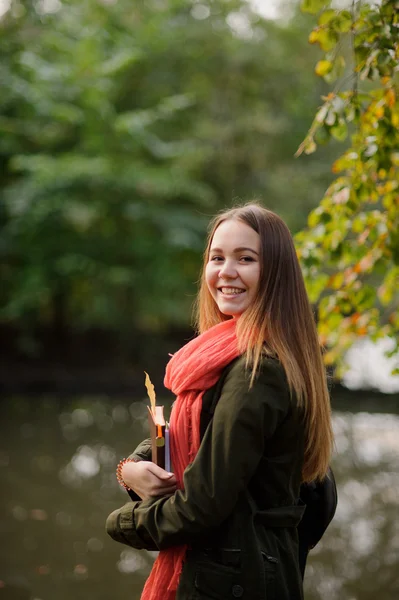 Mooi meisje in een helder rode sjaal wandelingen in herfst park. — Stockfoto