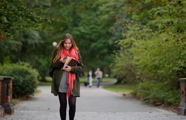 Młody student idzie w jesieni Park z zdejmowany telefon w ręku. — Zdjęcie stockowe