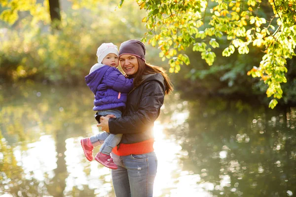 Jonge vrouw met een baby in haar armen kijkt naar de camera en glimlach. — Stockfoto