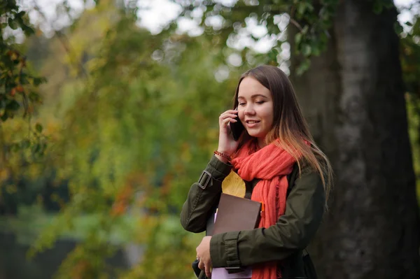 Lovely girl in bright red scarf is leaning against the trunk of a large tree. — Stock Photo, Image