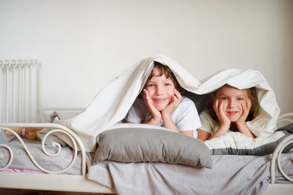 Little brother and sister made a play on the bed in the bedroom. — Stock Photo, Image