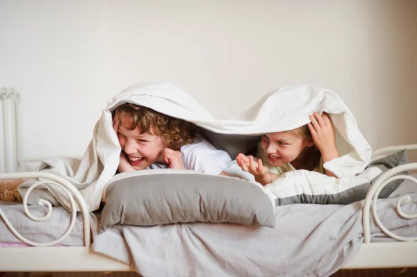 Little brother and sister made a play on the bed in the bedroom. — Stock Photo, Image