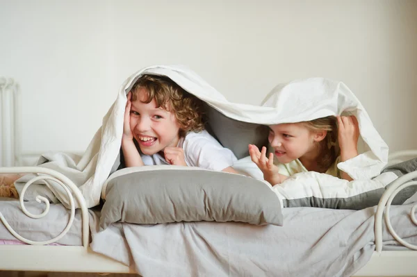 Little brother and sister made a play on the bed in the bedroom. — Stock Photo, Image