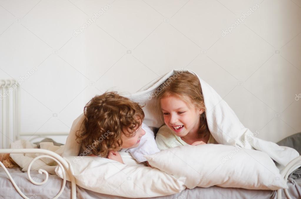 Two children, boy and girl, squirmy lying on the bed in the bedroom.