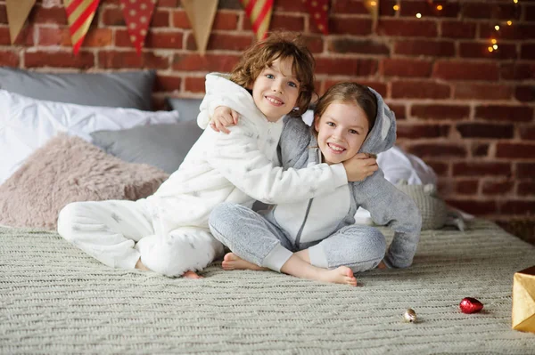 Due bambini in pigiama seduti sul letto in attesa di regali di Natale . — Foto Stock