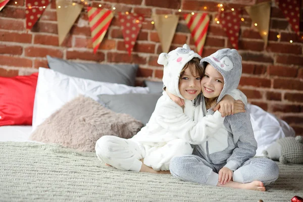 Zwei Kinder im Pyjama sitzen auf dem Bett und warten auf Weihnachtsgeschenke. — Stockfoto