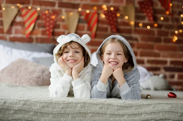 Weihnachtsferien. Bruder und Schwester liegen im weichen Schlafanzug auf dem Bett. — Stockfoto