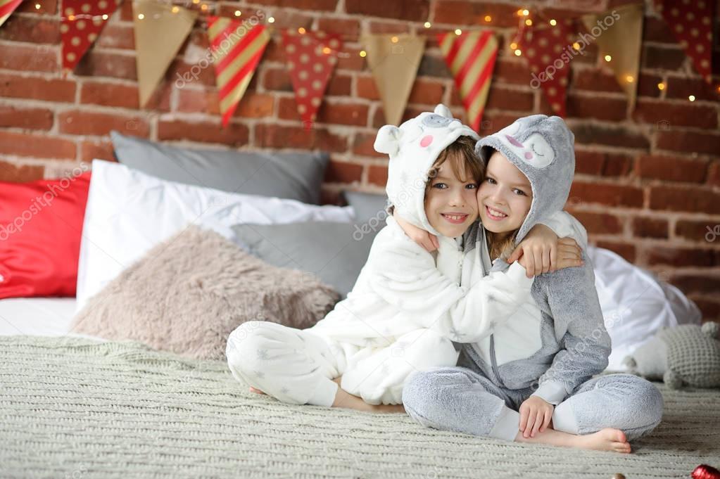 Two children in pajamas sitting on the bed waiting for Christmas gifts.