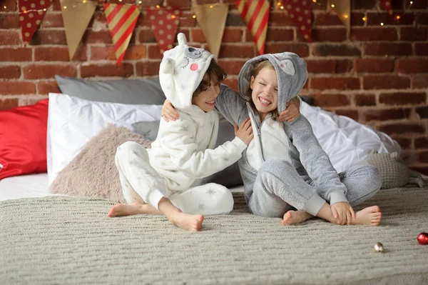 Zwei Kinder im Pyjama sitzen auf dem Bett und warten auf Weihnachtsgeschenke. — Stockfoto