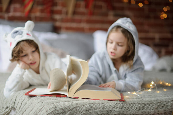 Двое детей лежат на большой кровати и читают сказки
.