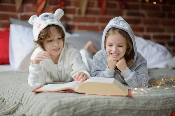 Deux enfants s'allongent sur un grand lit et lisent des contes de fées . — Photo