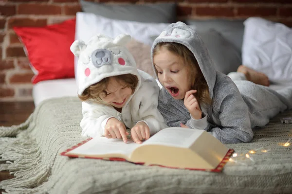 Deux enfants s'allongent sur un grand lit et lisent des contes de fées . — Photo