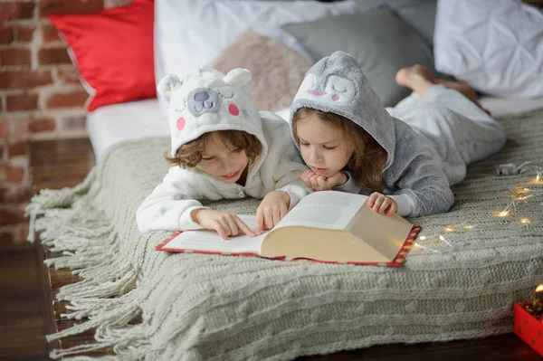 Deux enfants s'allongent sur un grand lit et lisent des contes de fées . — Photo