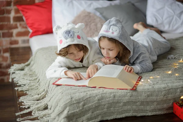 Dos niños se acuestan en una cama grande y leen cuentos de hadas . — Foto de Stock