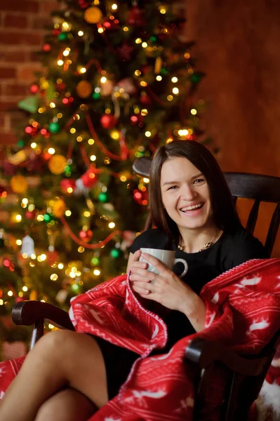 Mujer joven se sienta en una mecedora cerca del árbol de Navidad . — Foto de Stock