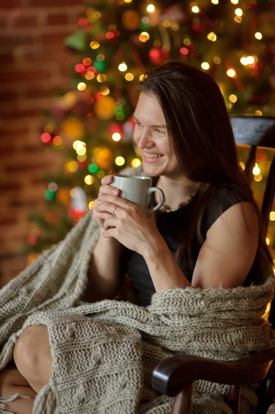 Mujer joven se sienta en una mecedora cerca del árbol de Navidad . — Foto de Stock