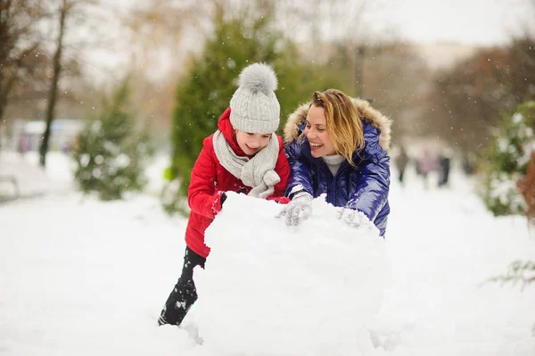 Mother with daughter of younger school age build a snowman in the park. — Stock Photo, Image