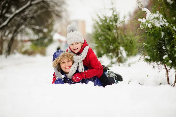 Jeune femme avec fille d'âge scolaire mensonge ayant embrassé sur la neige . — Photo