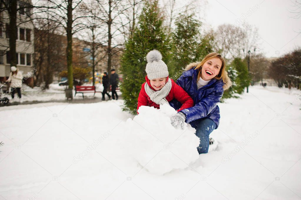 Mother with daughter of younger school age build a snowman in the yard.